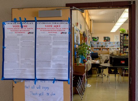 side by side signs taped to a door that "official polling place vote here" along with other text. One is in english and one in spanish. The open door leads into a school library