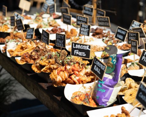 an array of dishes of food with little signs identifying some as lobster fries, lobster roll, honey walnut wings, asian wings, dirty piggy fries, garlic parmesan fries, wasabi wings