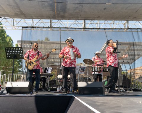 a band on stage of four latino men in matching red hawaiian shirts with white flowers