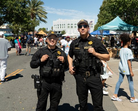 two police officers, one smiling and one wearing sunglasses and not smiling