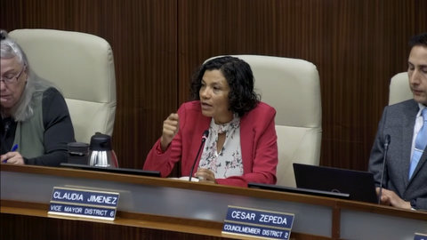 latina woman with nameplate that identifies her as claudia jimenez vice mayor district 6. to her right is a latino man in a suit with a nameplate that reads cesar zepeda councilmember district 2. to her left is an older white woman. her nameplate is not visible but she is council member gayle McLaughlin