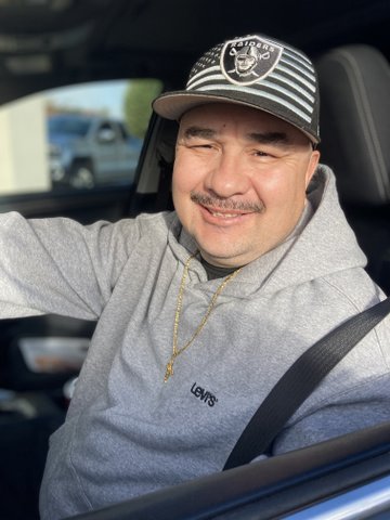 latino man in driver's seat wearing raiders cap