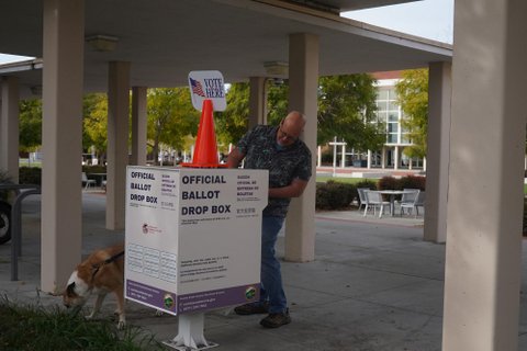 a white man with a dog at an official ballot drop box