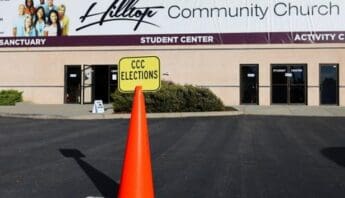 orange cone in a handicapped parking spot with a yellow sign that reads CCC elections in front of a building with a sign that reads hilltop community church