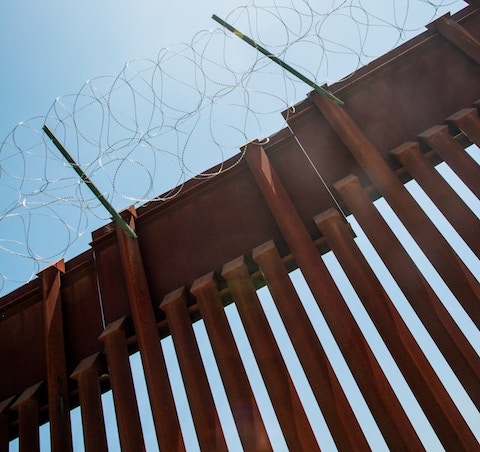 looking up at a border fence topped with barbed wire