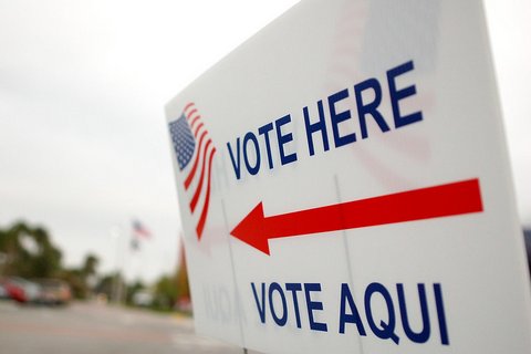 sign that reads vote here vote aqui with red arrow and US flag illustration