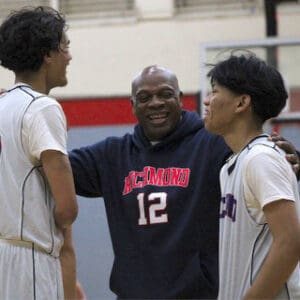 a black man in a Richmond number 12 hoodie standing between two high school basketball players