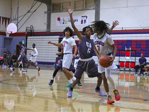 high school basketball player with the ball looks past a defender with arms raised high