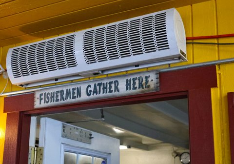 a sign that reads "fishermen gather here" below a large vent and above a doorway