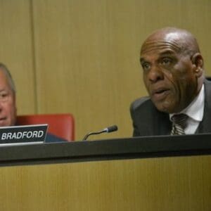 black man in a suit sitting at a microphone and nameplate that says steven bradford. a white man is next to him