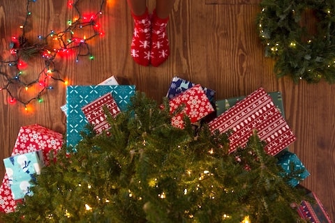 looking down toward a partial view of a christmas tree with presents under it and a child's feet in red socks pointing toward the tree