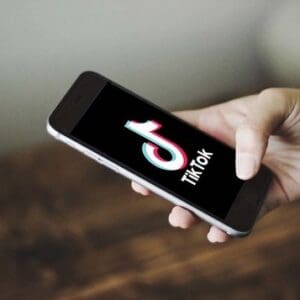 a white hand holding a black smartphone with the words tik tok and the app's logo