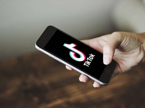 a white hand holding a black smartphone with the words tik tok and the app's logo