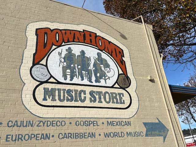 "Down Home music store cajun zydeco gospel mexican european caribbean world music" painted on beige brick wall with illustration of three seated musicians