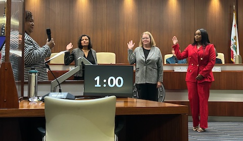 a latina woman, white woman and black woman being sworn into a city council by a black woman