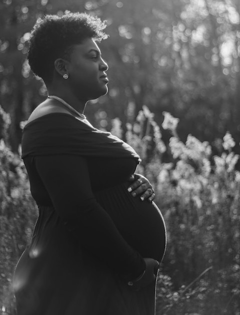 grayscale photo showing side view of a pregnant black woman with her hands cradling her belly