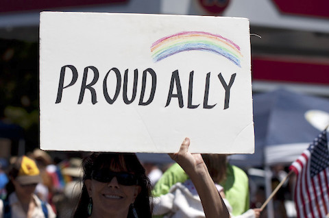 woman holding up sign that says proud ally with a rainbow drawn on it