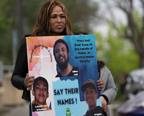 black woman holding poster board with photos of miles hall, laudemer arboleda and angelo quinto and text that reads say their names, they lost their lives at the hands of police in contra costa county. mental illness is not a crime