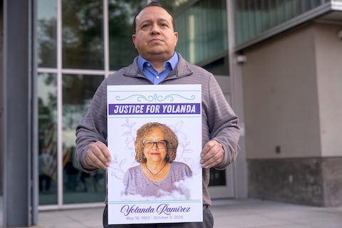 latino man holding poster with photo of latina woman and text that reads justice for yolanda yolanda ramirez may 16, 1953 - october 3, 2025