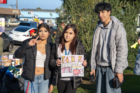 a young woman flashing a peace sign, a young woman holding a sign that reads teachers need more than apples with a drawing of a red apple