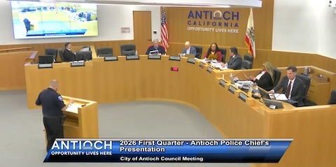 white man in police uniform standing at a lectern facing members of city council and staff of which 2 are black women and the rest are men. text reads 2026 first quarter antioch police chief's presentation, city of antioch council meeting